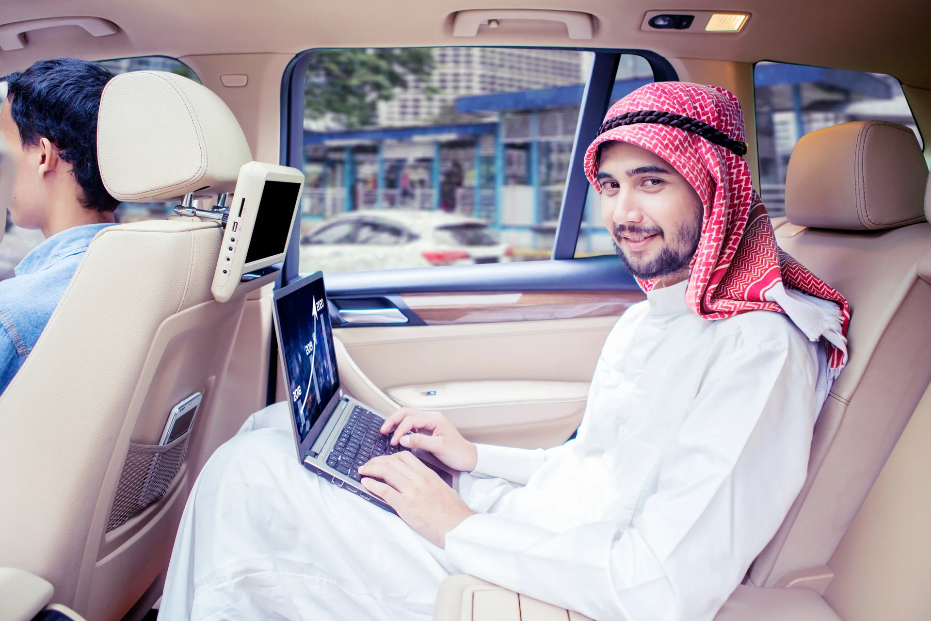 Arabian man works with laptop while smiling in car