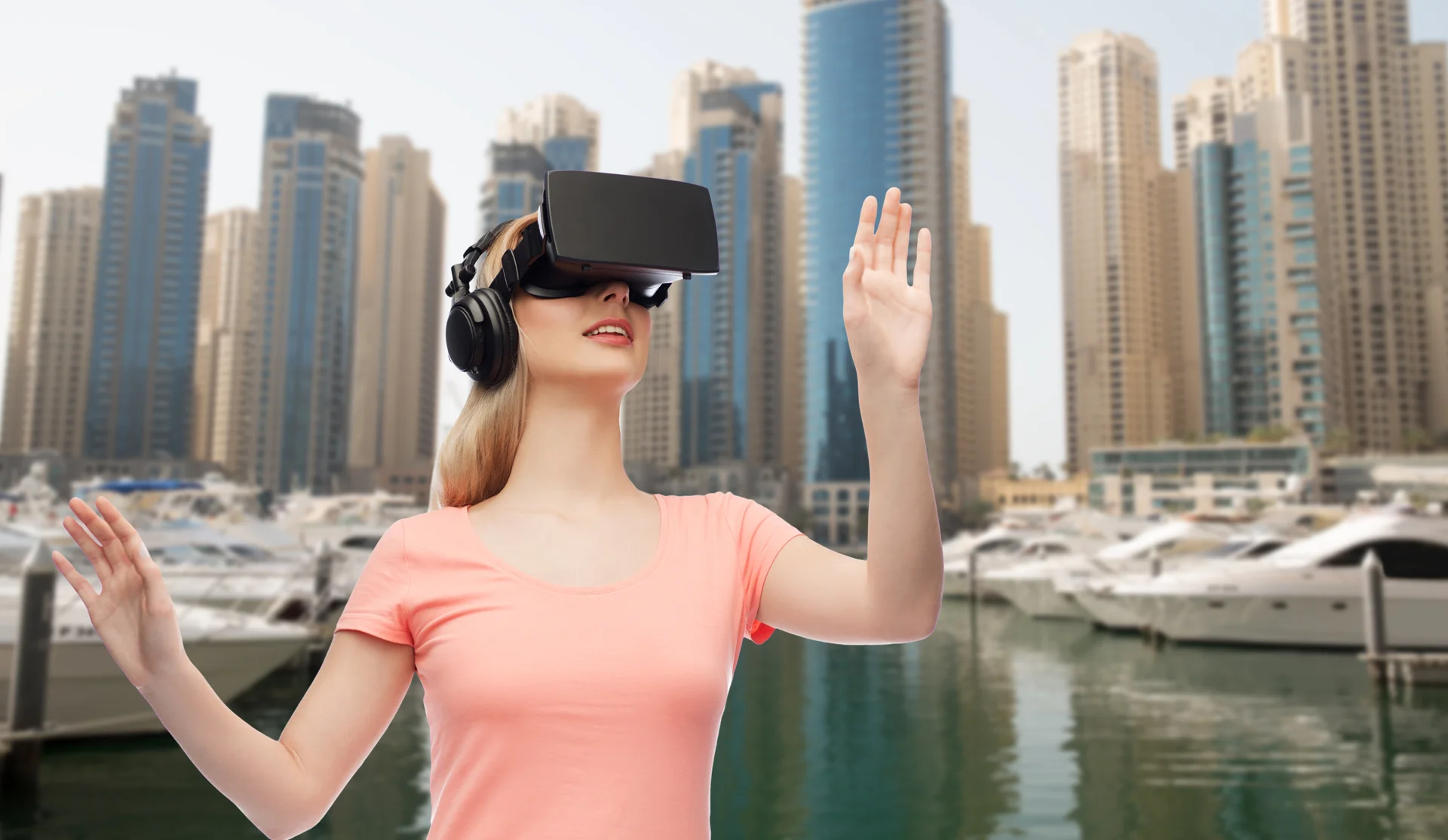 technology, virtual reality, entertainment, travel and people concept - happy young woman with virtual reality headset or 3d glasses and headphones playing game over dubai city street background