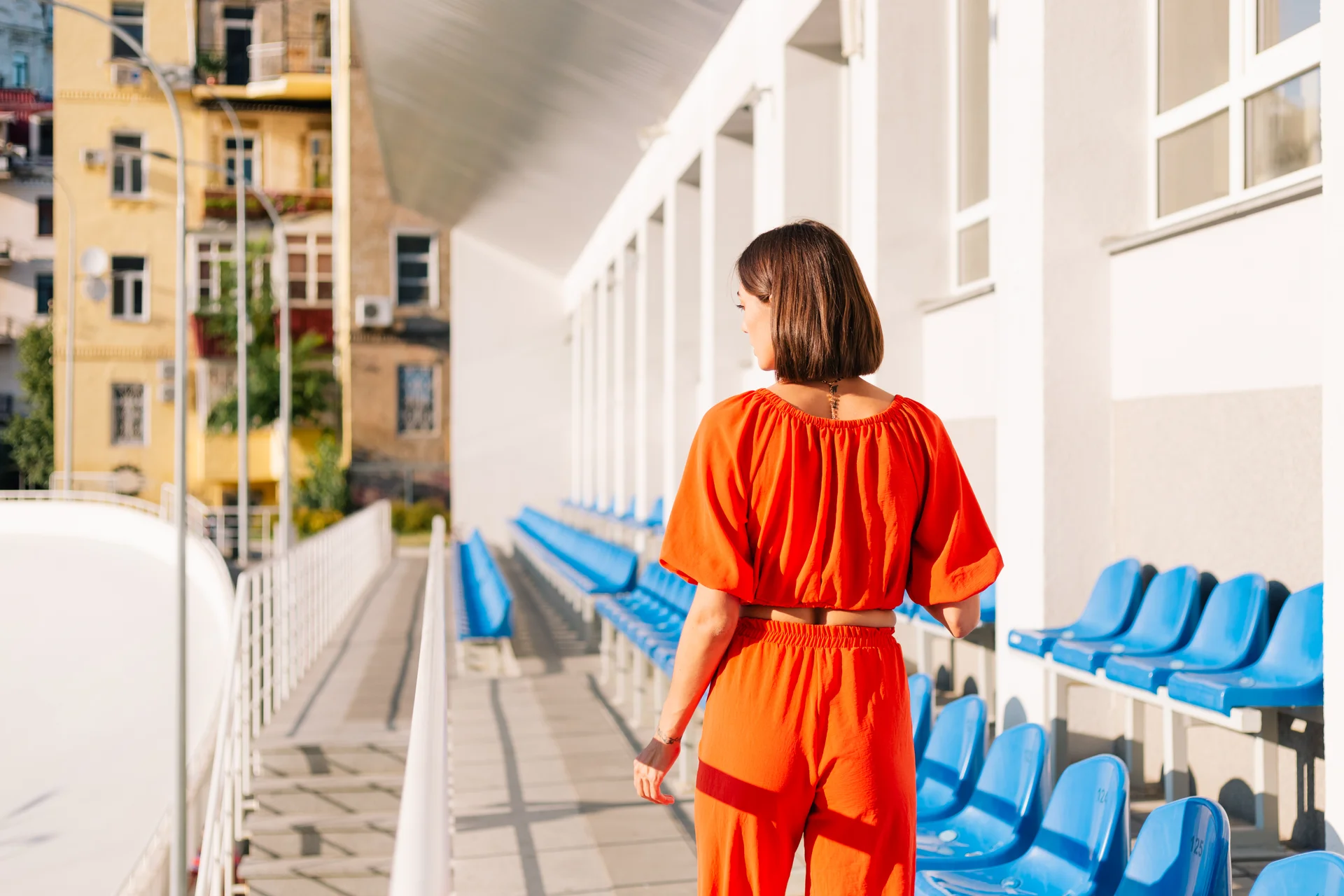 Stylish woman in orange clothes at sunset at cycle track stadium posing
