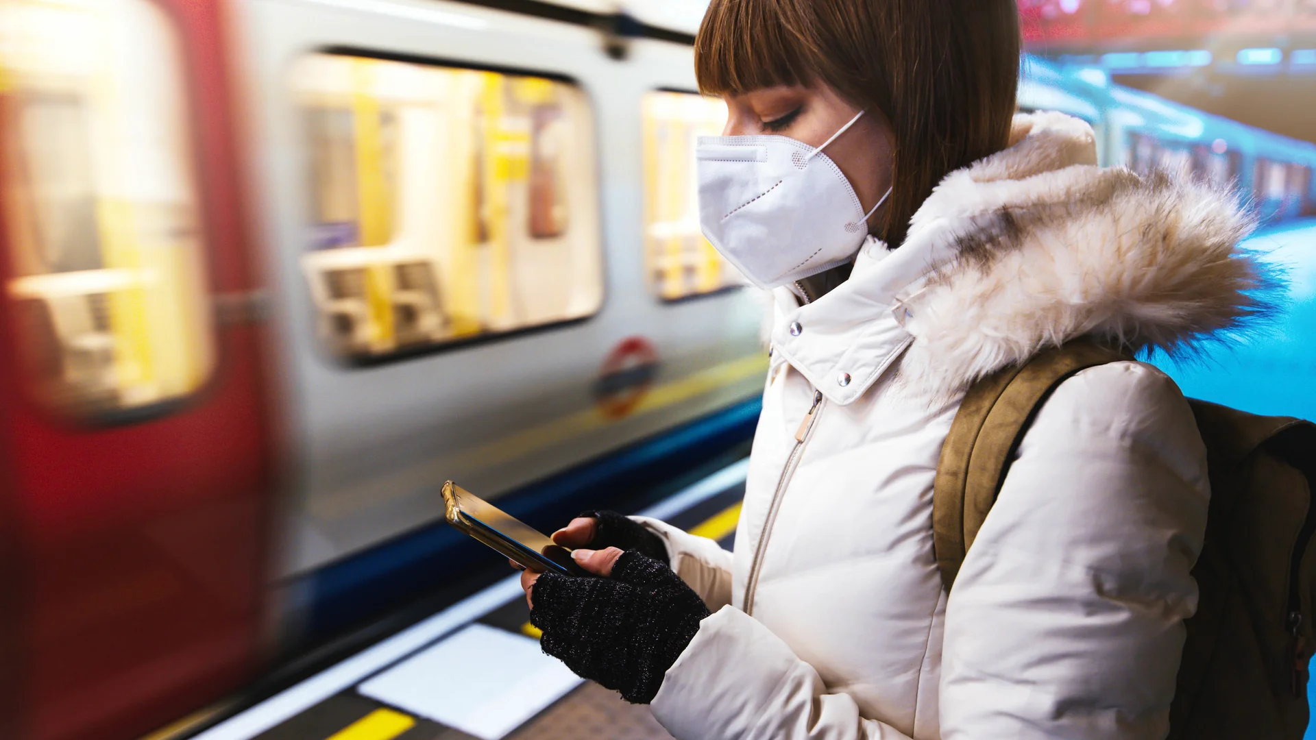 Young woman wearing protective face mask using smart phone device on London underground