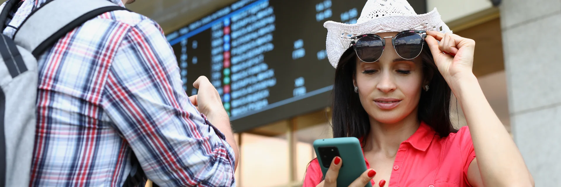 Man and woman are tourists with mobile phone against background of electronic board of bus and railw
