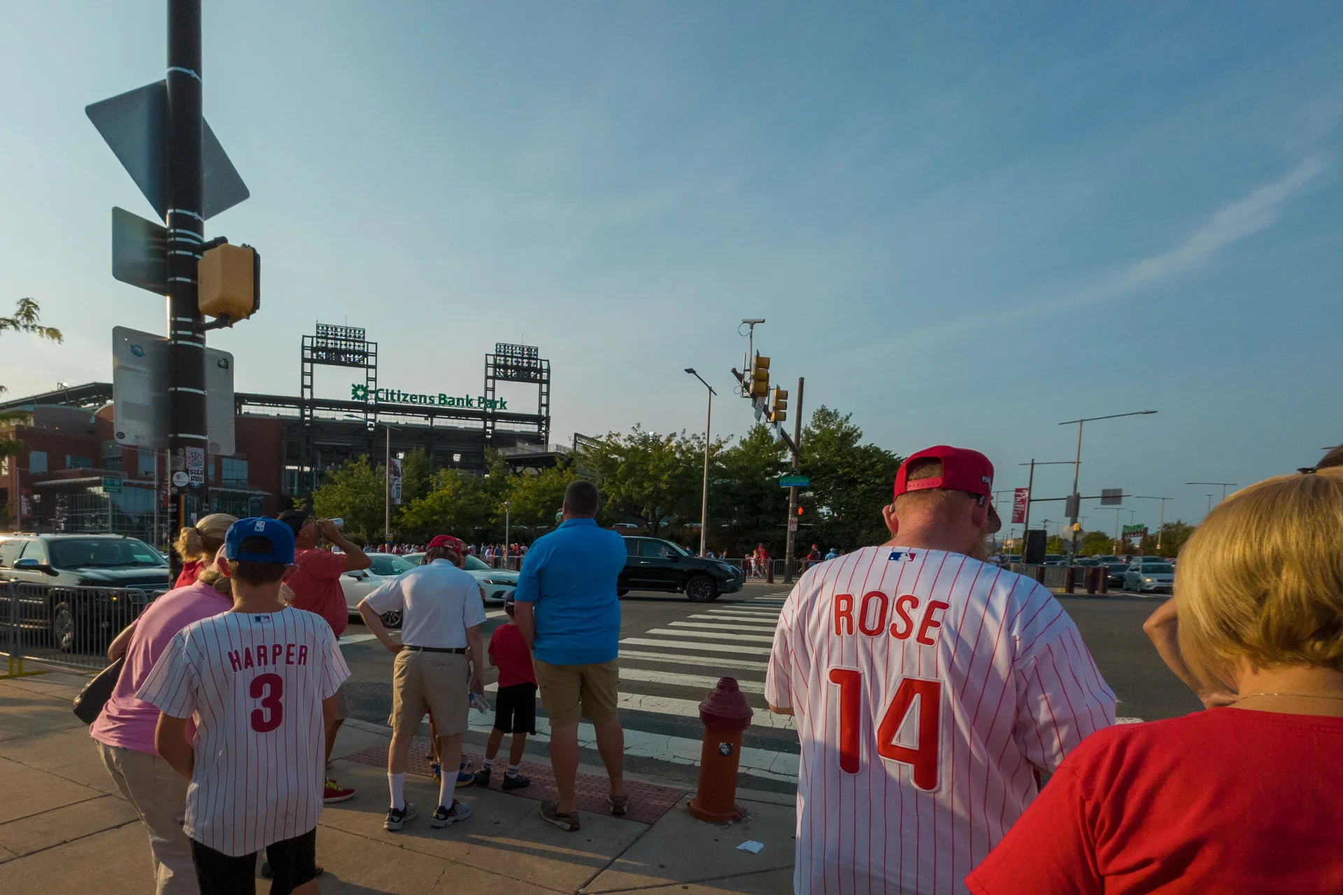 A group of people are standing on a street some wearing Philadelphia Phillies jerseys