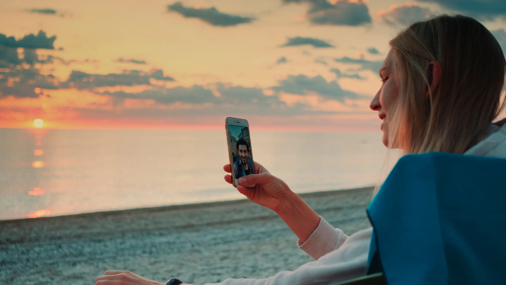 Young woman making video call to her friend with smartphone on the beach