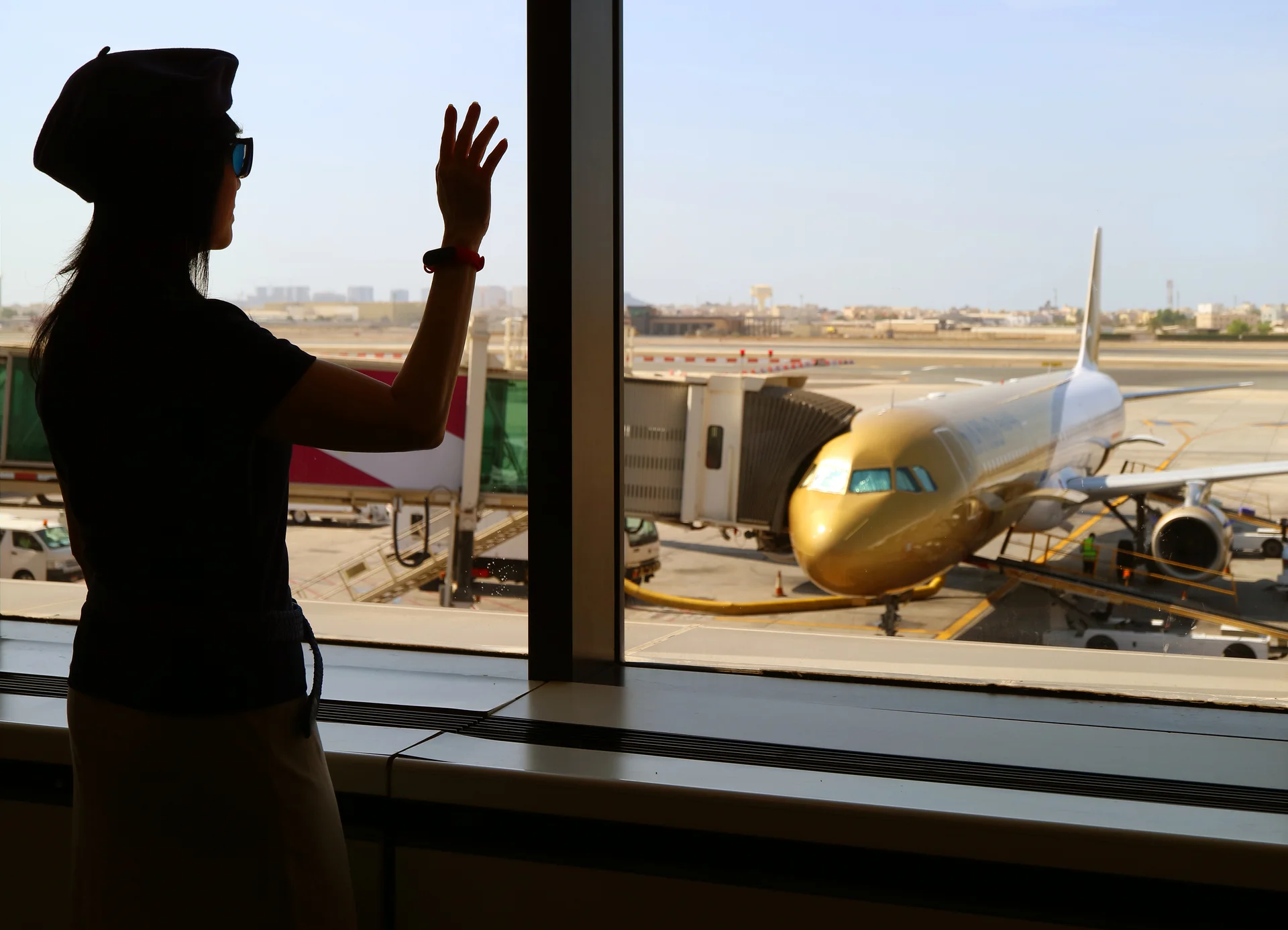 Silhouette of a woman waving hand to the airplane at the airport